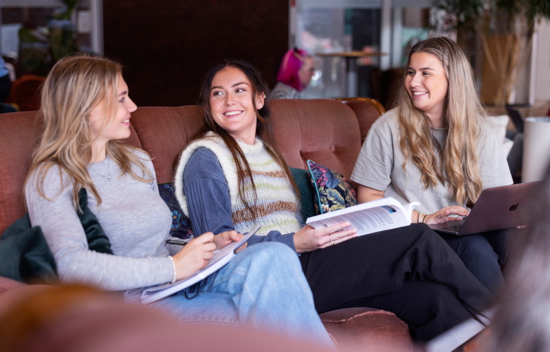 Tre studenter sitter i en sofa og snakker.