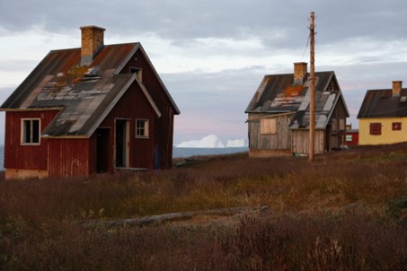 Tin roofed houses in red and yellow with icebergs on the sea in the background