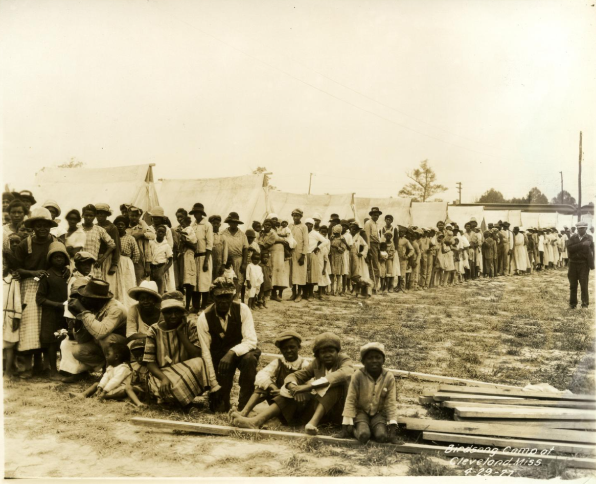 A queue of people with tents in the background