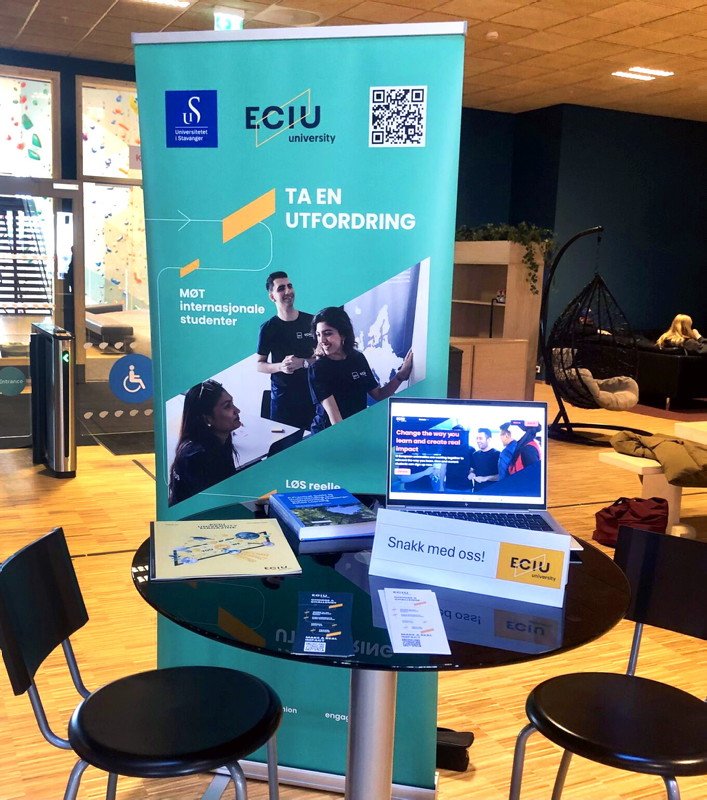 Cafebord med trykksaker og banner bak som reklamerer for ECIU University