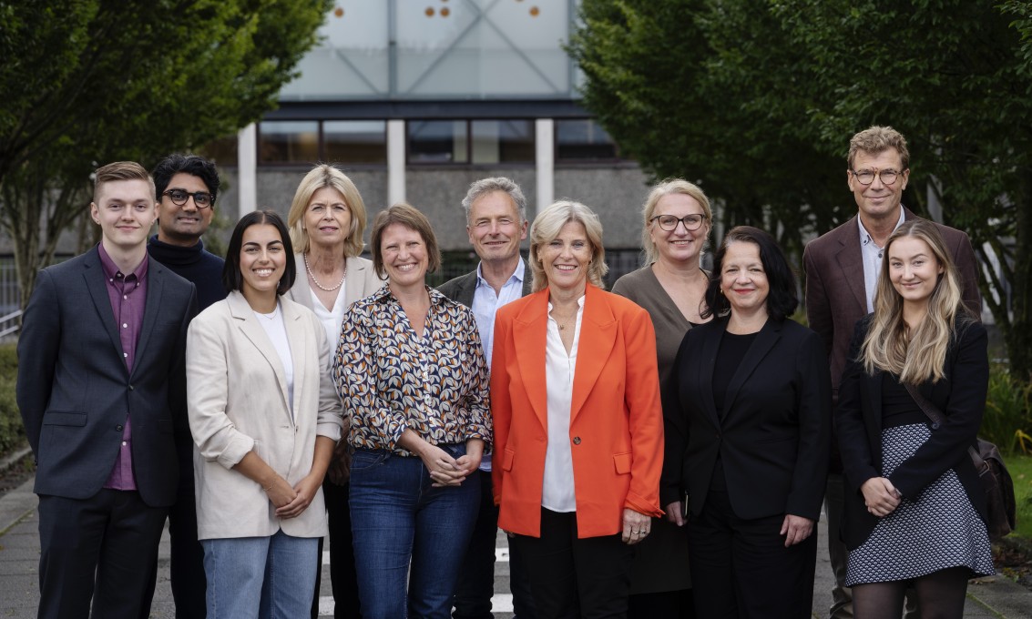 Styret ved UiS for 2023-2027 oppstilt for gruppebilde utendørs med bygning og grønne trær i bakgrunnen.