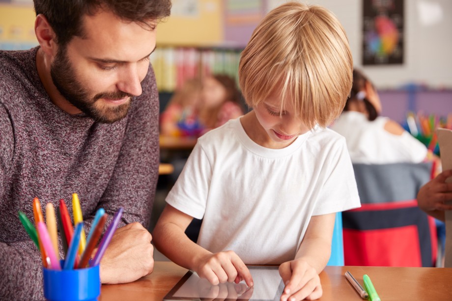 Mannlig lærer hjelper elev med i-pad i et klasserom