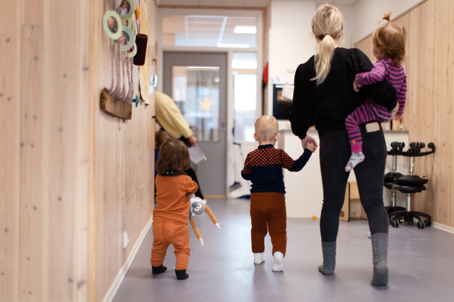 Voksen person går i gang med tre barn. Hun holder den ene i hånden og en annen på hofta