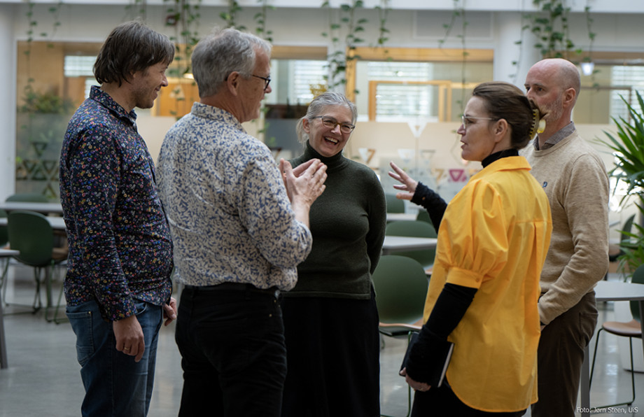 Fem voksne står i en sirkel og snakker sammen