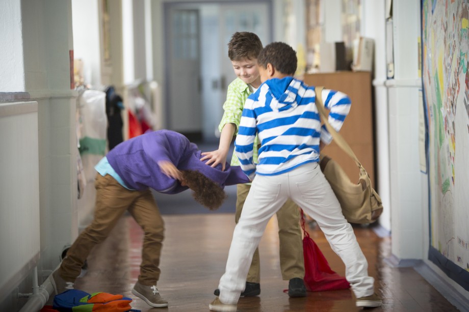 To gutter dytter hodet til en tredje gutt mot gulvet. De befinner seg i en gang på en skole. 
