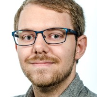 Portrettbilde av mann med briller som smiler til kamera. Foto. 